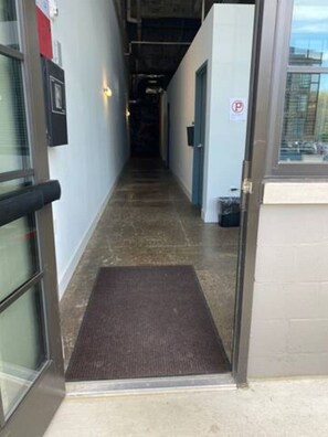 A hallway with a doormat, a door with a 'No Parking' sign, and a window with blinds.