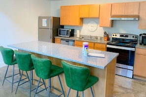 A kitchen with a granite countertop, stainless steel appliances, wooden cabinets, and green bar stools. - The coolest loft in Cincinnati Area (Maineville)