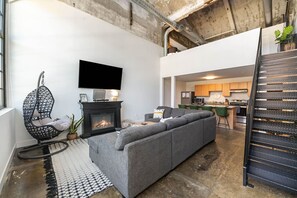 A living room with a grey sofa, a hanging chair, a fireplace, and a TV mounted on the wall.