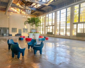 A spacious indoor area with large windows, a high ceiling, and several seating areas with colorful stools.