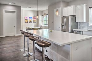 A modern kitchen with white cabinetry, a large island with bar stools, stainless steel appliances, and pendant lighting.