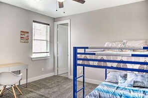 A bedroom with a bunk bed, a desk, a chair, and a window with blinds.