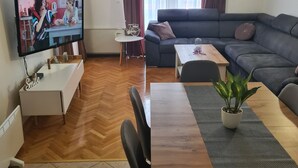 Ein modernes Wohnzimmer mit Fernseher, Sofa, Esstisch und einem kleinen Tisch mit einer Pflanze.
