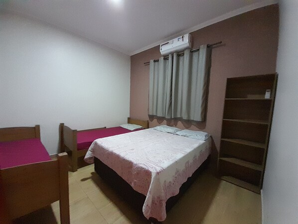 A small bedroom with two single beds, a wooden chair, a wardrobe, and an air conditioning unit. - Casa Temporada Amélia- Olímpia Interior SP (Olímpia)