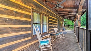 Uma cabana de madeira com varanda, cadeiras de balanço e ventilador de teto.