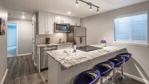 A modern kitchen with a granite countertop, stainless steel appliances, and a bar stool seating area. - Fully stocked new apt, work from home + Free Parking! (Denver)