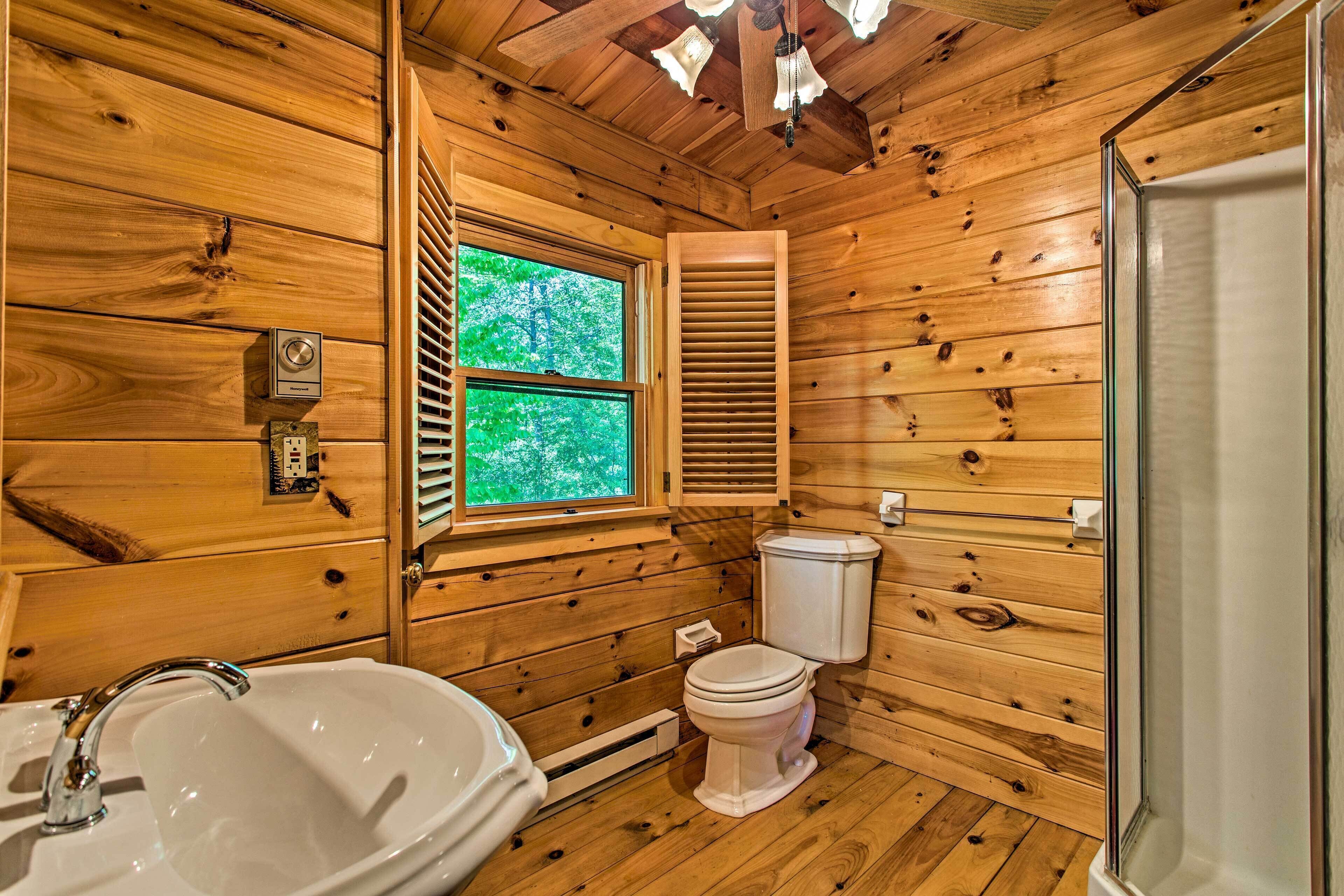 A wooden cabin bathroom with a sink, toilet, and window.