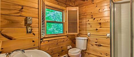 A wooden cabin bathroom with a sink, toilet, and window.