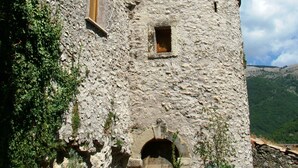 A stone tower with arched windows and a small door, surrounded by greenery and hills. - Amazing Lake View (Castel di Tora)