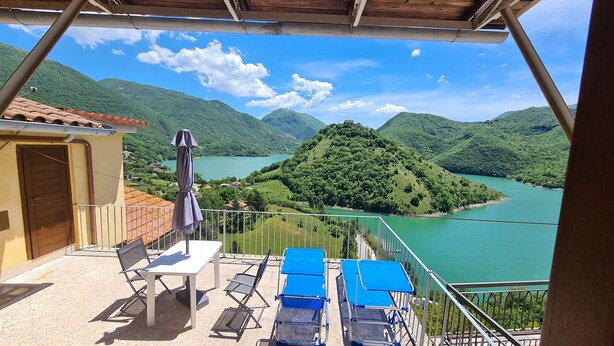 A balcony with a table and chairs, overlooking a lake and green hills. - Amazing Lake View (Castel di Tora)