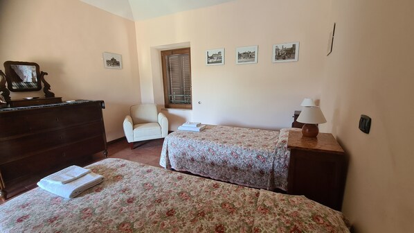Una camera da letto con due letti singoli, una cassettiera in legno, una sedia e una finestra con persiane.