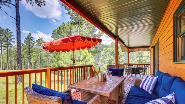 A covered deck with wicker furniture, a table, and an umbrella. - Keystone Escape w/ Amazing Mt Rushmore View! (Keystone)
