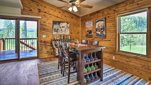 A wooden interior with a dining table, chairs, a ceiling fan, and large windows offering a view of the outdoors. - Keystone Escape w/ Amazing Mt Rushmore View! (Keystone)