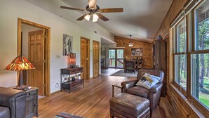 A spacious living room with wooden floors, a ceiling fan, and large windows offering a view of the outdoors. - Keystone Escape w/ Amazing Mt Rushmore View! (Keystone)