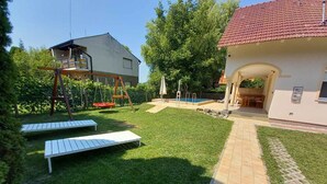 A backyard with a swimming pool, a swing set, and a patio area. - Holiday home with pool and garden shower (Badacsony)