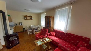 A living room with a red sofa, a wooden coffee table, a fireplace, a dining area with a table and chairs, and a kitchen area with a stove and cabinets. - Holiday home with pool and garden shower (Badacsony)