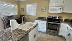 A kitchen with white cabinets, a stainless steel dishwasher, a granite countertop, a microwave, an oven, and a ceiling fan. - Waterfront Home in Gulf Harbors with Deepwater Access to Gulf with No Bridges (New Port Richey)