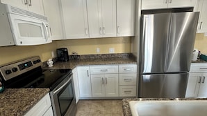 A kitchen with white cabinets, stainless steel appliances, granite countertops, and pendant lighting. - Waterfront Home in Gulf Harbors with Deepwater Access to Gulf with No Bridges (New Port Richey)