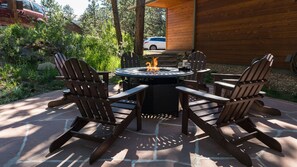 A patio with Adirondack chairs around a circular fire pit table, surrounded by a wooden deck and a stone patio. - Family Gathering Home! Beautiful, Spacious, Clean! Next to Rocky Mtn N.P., YMCA (Estes Park)