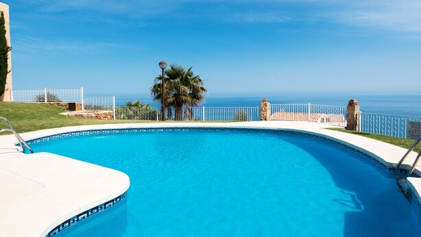Piscina con vista despejada al océano, rodeada por una cerca blanca y palmeras.