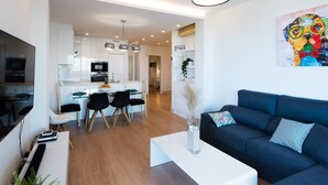 Una sala de estar moderna con un sofá negro, una mesa de centro blanca y una zona de comedor con una mesa y sillas de vidrio.