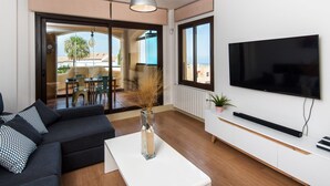 Una sala moderna con un sofá, una mesa de centro, un televisor y un ventanal corredizo que da a un espacio exterior.