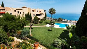Un edificio de estilo mediterráneo con piscina, rodeado de vegetación exuberante y vistas al mar.