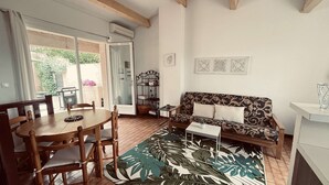 A living room with a wooden dining table, chairs, a patterned sofa, and a large tropical leaf rug. - Mazet for 6 people in a domain with pool and tennis court in Cogolin (COGOLIN)
