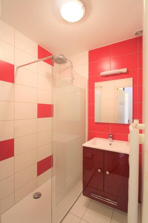 Bathroom features a glass-enclosed shower, sink, and mirror, along with a red cabinet and towel storage.