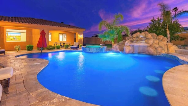 Une piscine avec un jacuzzi, une maison avec un toit en tuiles et un ciel au coucher du soleil.