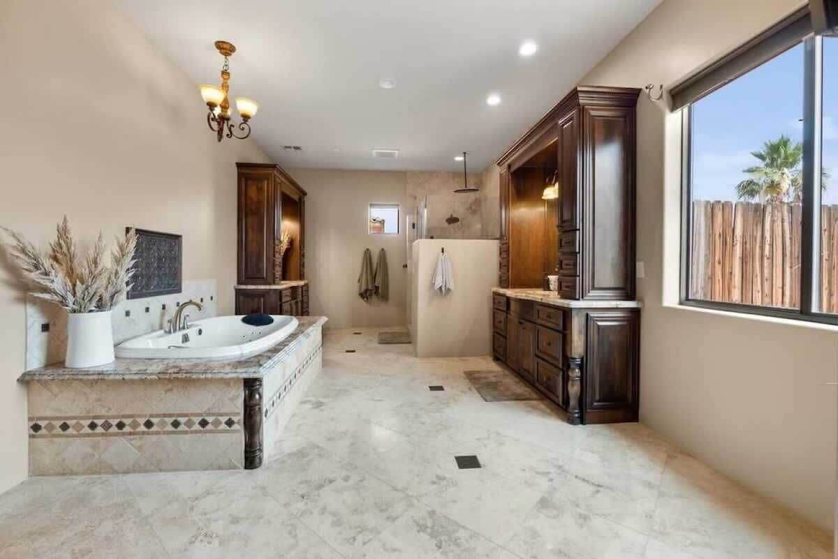 Ruime badkamer met een groot bad, houten kastjes en een groot raam met uitzicht op de omgeving.