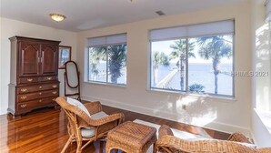A room with a wooden cabinet, wicker furniture, and large windows with a view of palm trees and a dock. - Dreamworthy, waterfront St. Helena home with pool and deep water dock. (St. Helena)