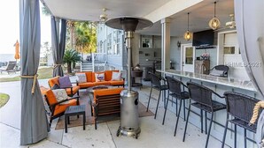 An outdoor patio area with a sofa, chairs, a grill, and a bar with stools. - Dreamworthy, waterfront St. Helena home with pool and deep water dock. (St. Helena)