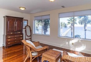 A room with a wooden cabinet, wicker furniture, and large windows with a view of palm trees and a dock. - Dreamworthy, waterfront St. Helena home with pool and deep water dock. (St. Helena)
