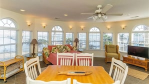 A spacious living room with a wooden dining table, white chairs, a sofa with a floral cover, and a television on a wooden cabinet. - Dreamworthy, waterfront St. Helena home with pool and deep water dock. (St. Helena)