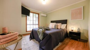 Une chambre à coucher comprenant un lit, une table de chevet, une lampe, une fenêtre avec des stores et un climatiseur fixé au mur.