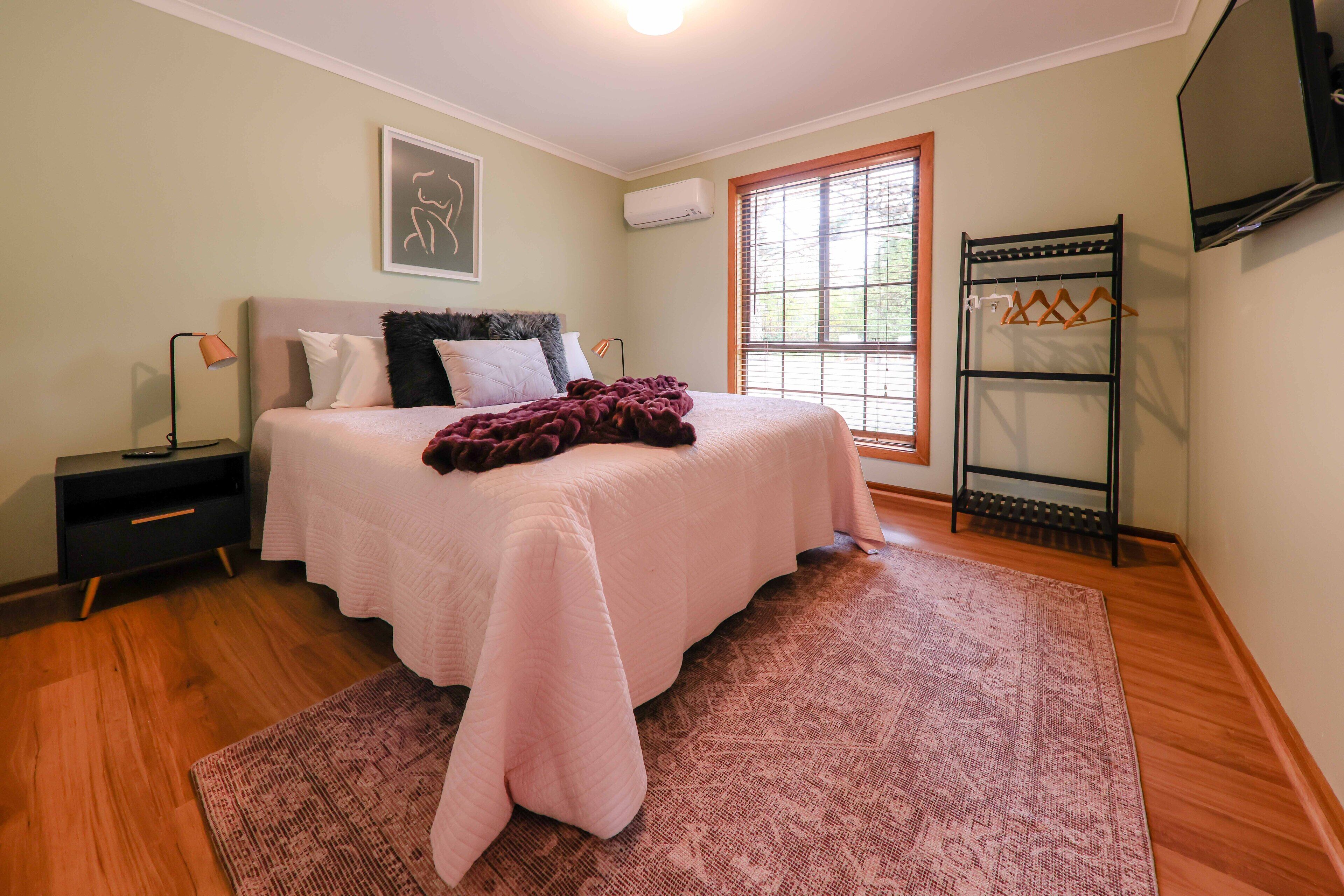 Un dormitorio con una cama, una mesita de noche, una lámpara, una ventana y un televisor.