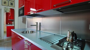 A modern kitchen with stainless steel appliances, a double sink, and red cabinetry. - GetTheKey Boldrini Loft 2 (Bologna)
