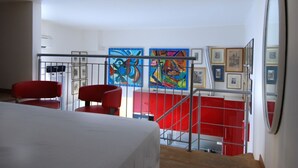 A hotel room with a bed, two red chairs, a staircase with red railings, and colorful artwork on the walls. - GetTheKey Boldrini Loft 2 (Bologna)