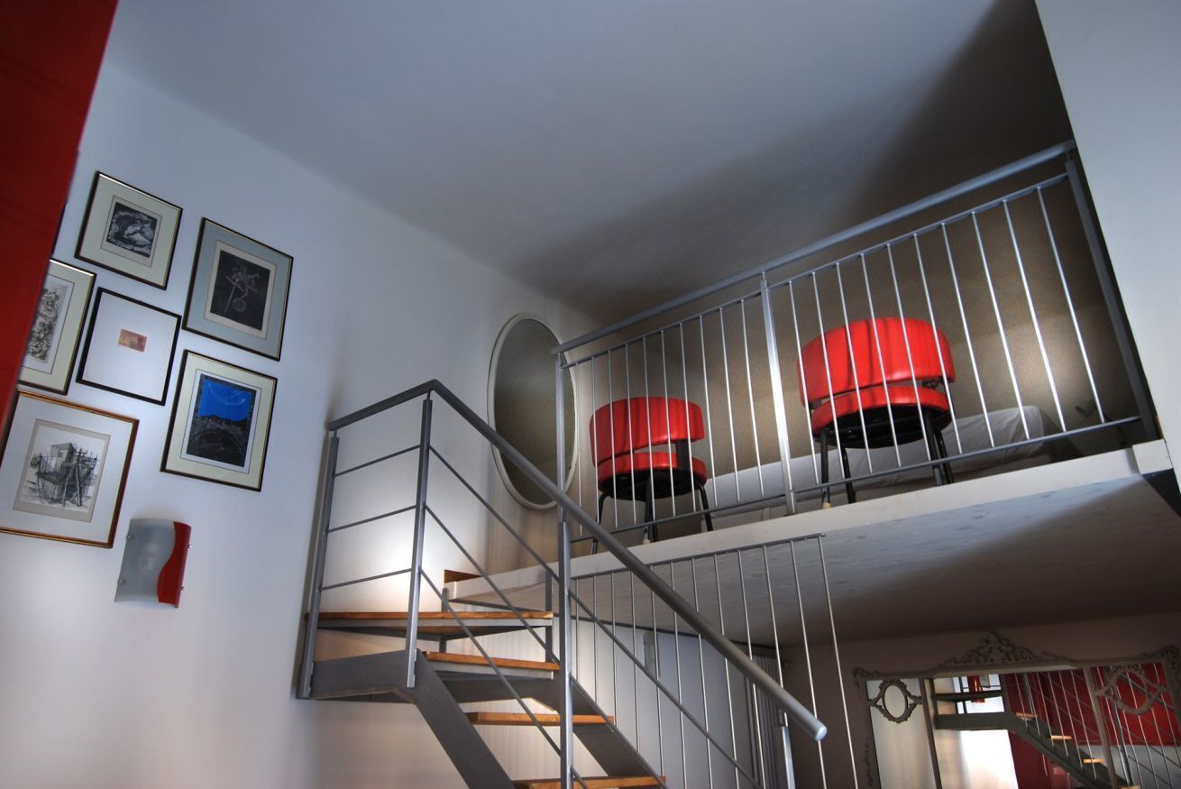 Una escalera con barandillas de metal que lleva a un balcón en el segundo piso con una silla roja.