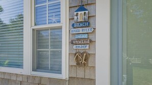 Een huis met een raam en een bord aan de muur waarop staat: ‘BEACH HOUSE RULES relax unwind enjoy’.