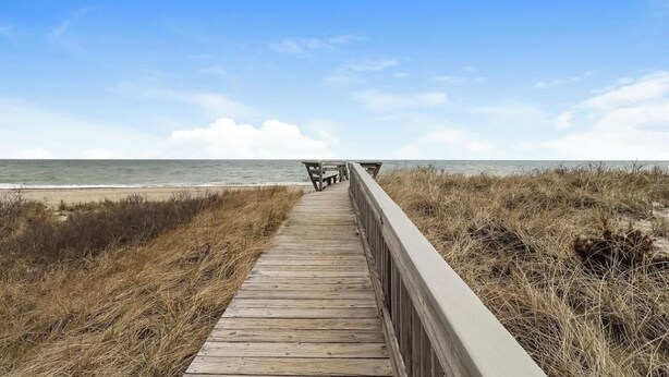 Een houten looppad dat naar een strand leidt, met een bank aan het einde.