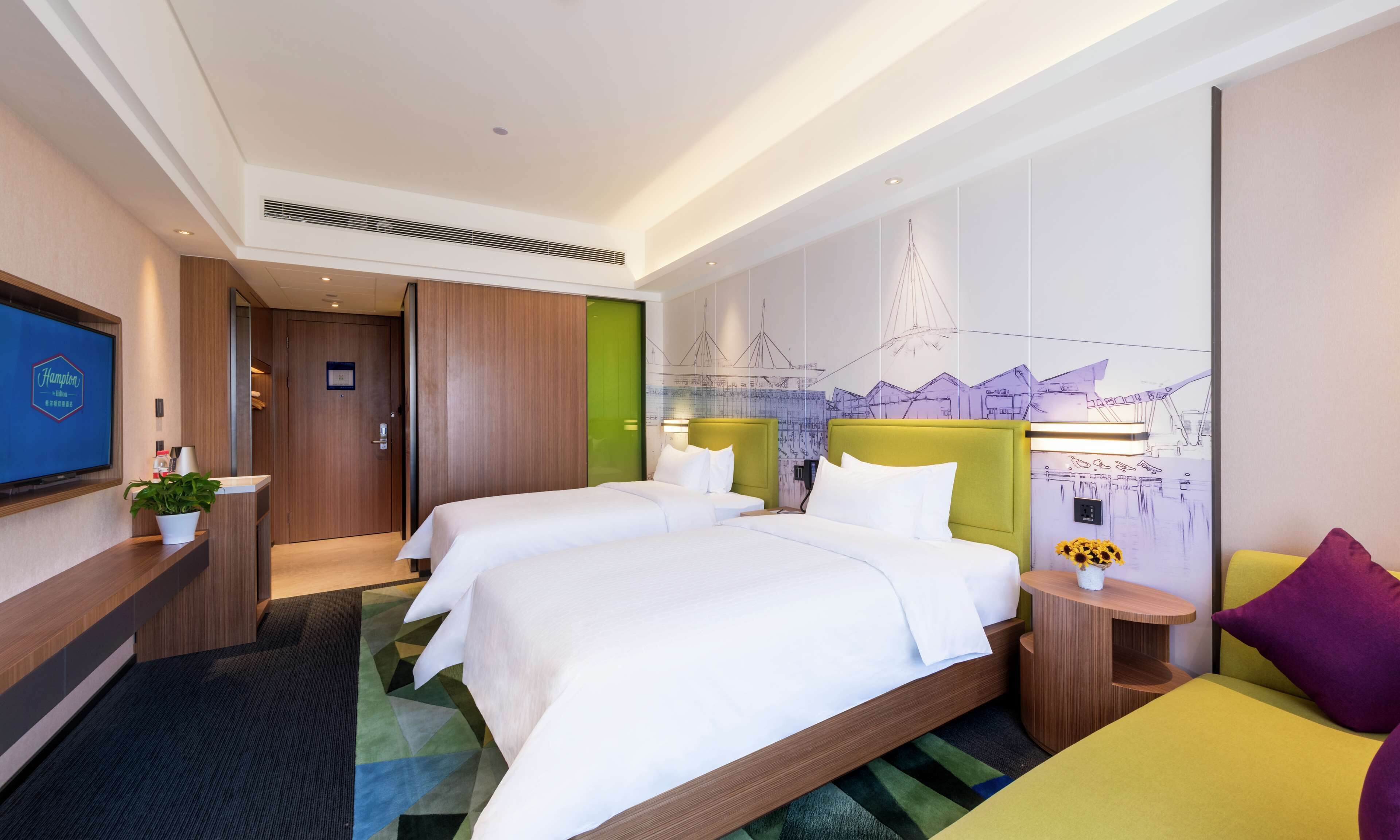 A hotel room with two beds, a TV, a desk, and a cityscape mural on the wall.