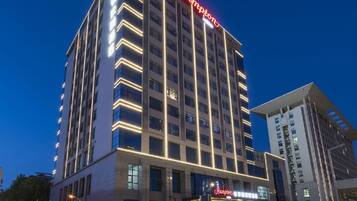 A multi-story hotel with a prominent red sign, a modern facade, and a well-lit entrance.