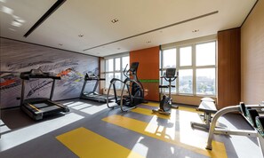 Un gimnasio moderno con cintas de correr, elípticas y una bicicleta estática. Amplios ventanales ofrecen vistas a la ciudad.