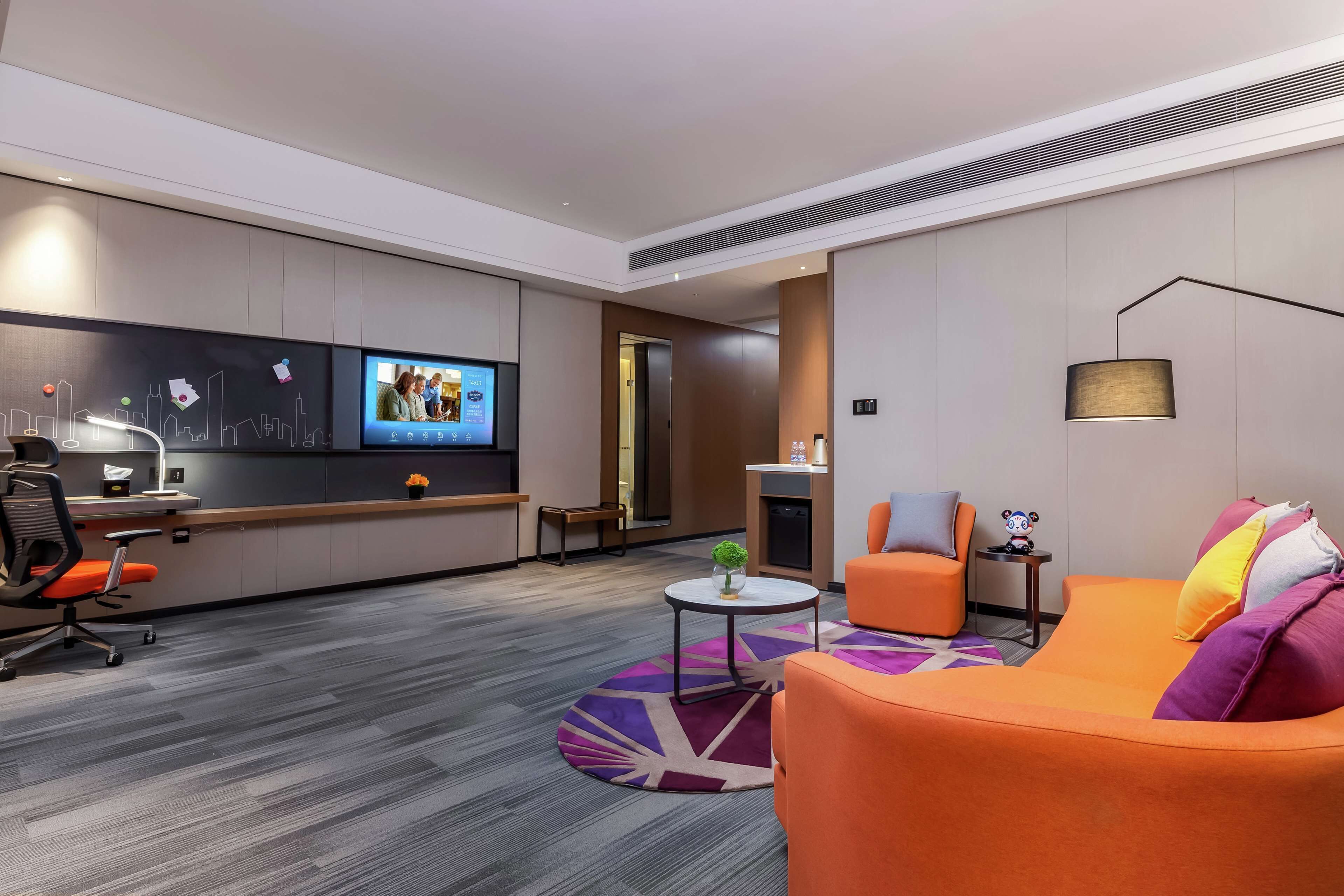 Habitación de hotel moderna con sofá, una mesita, televisor y escritorio con silla.