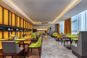 Ein modernes Restaurant mit hohen Tischen und Stühlen, einer langen Theke und Blick auf die Stadt durch große Fenster.