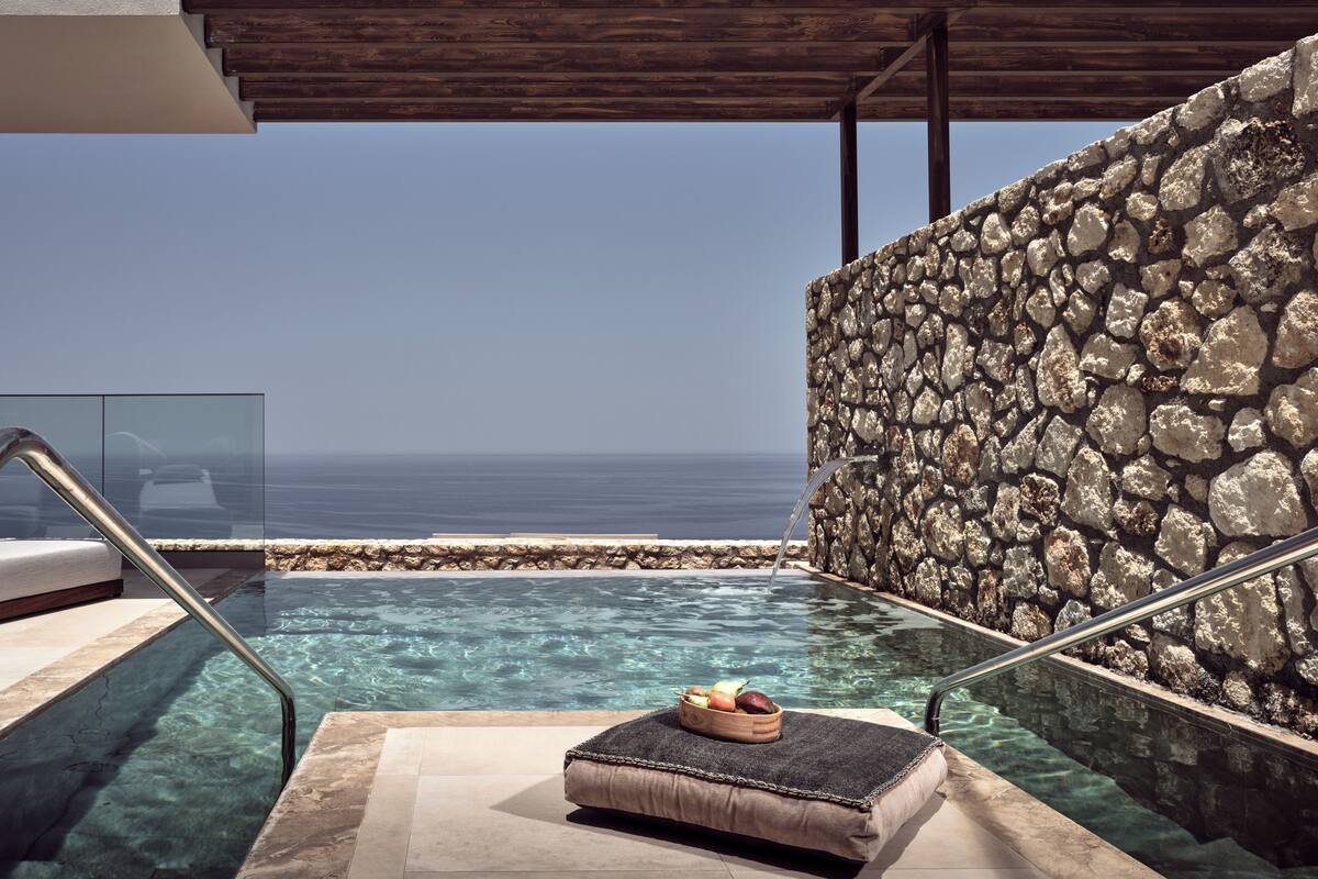 A private infinity pool with a stone wall and a wooden deck, overlooking the ocean.