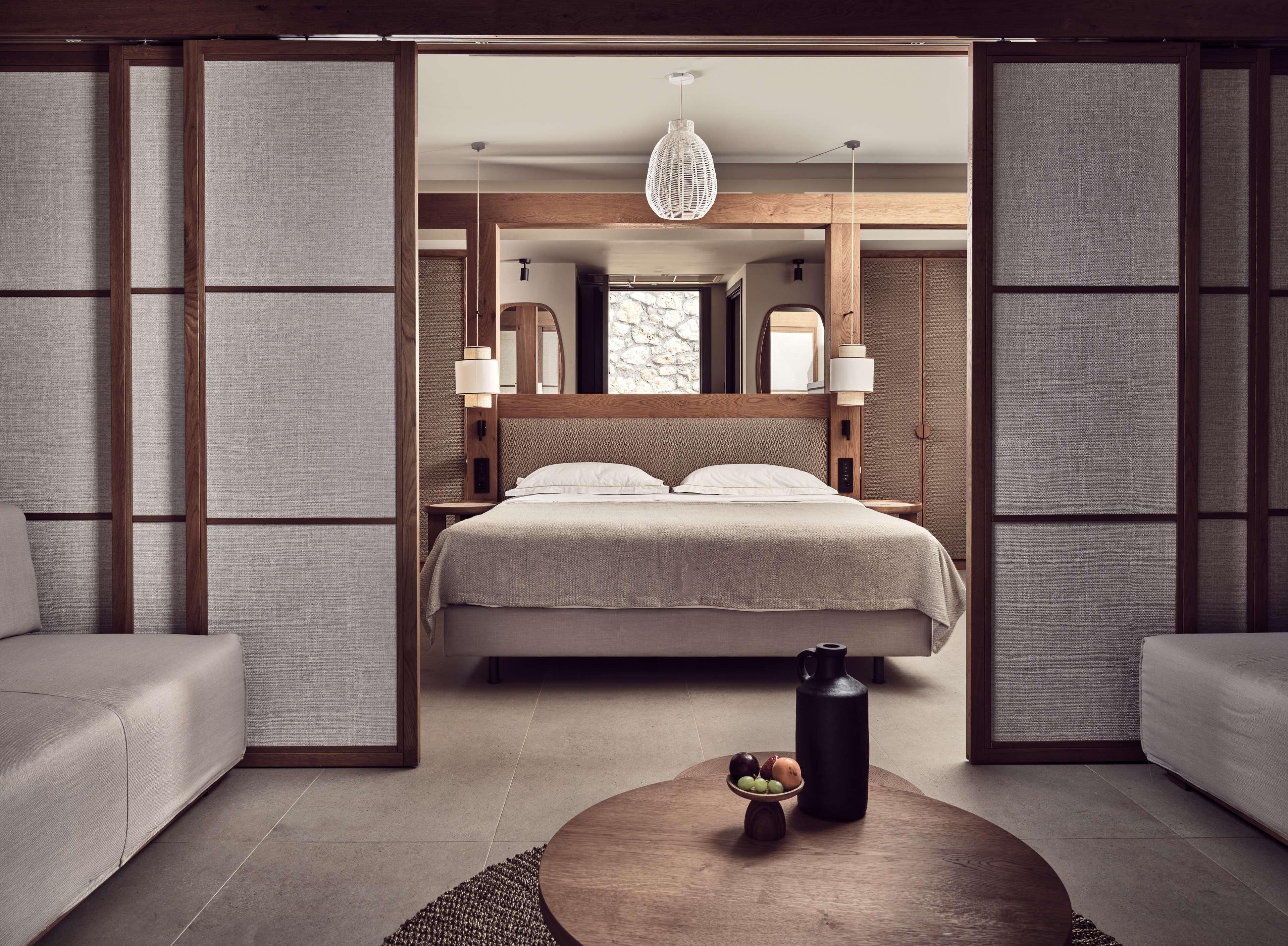 Une chambre à coucher moderne avec un lit, des tables de chevet, un luminaire suspendu et une table basse sur laquelle sont disposés des fruits.