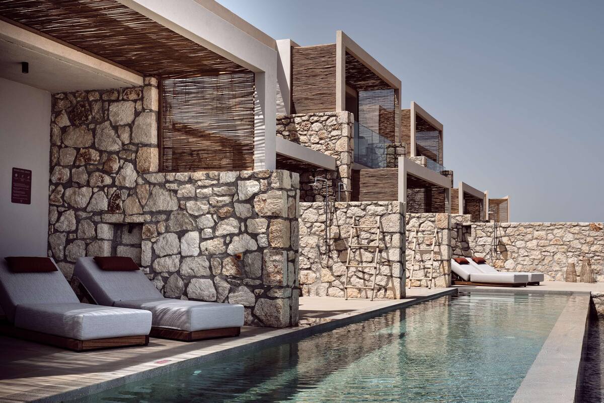 A modern poolside area with stone walls, lounge chairs, and a clear pool.